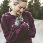 selective focus photography of woman wearing purple sweater holding silver tabby cat